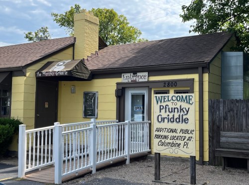 A yellow building with a sign reading "Welcome to Pfunky Griddle" and an open door, featuring a white railing.