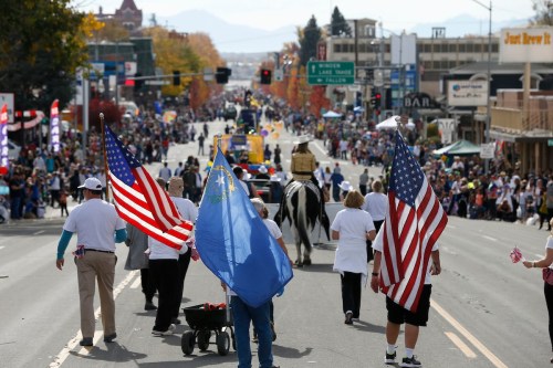 A parade scene with participants holding American and state flags, walking down a busy street lined with spectators.