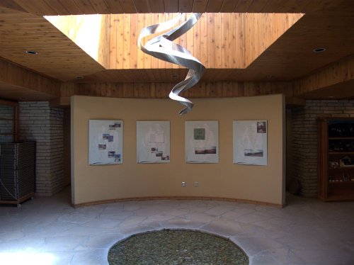 Interior view of a room featuring a spiral sculpture, skylight, and display boards on a curved wall.