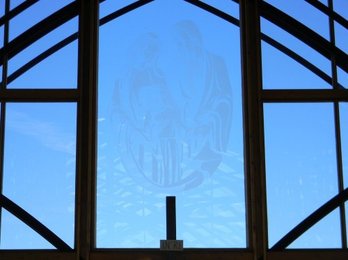 A large window with a blue sky background, featuring a faint etched image of two figures.