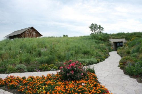 A winding stone path leads through colorful flowers to a grassy hill with a modern building at the top.