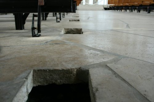Close-up of a stone floor with irregular holes, showing a modern architectural design in a spacious interior.