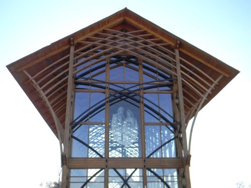 A modern wooden structure with a large glass facade and a distinctive peaked roof against a clear sky.