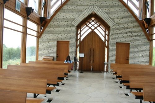 A serene interior of a modern chapel with wooden benches and large windows, featuring a person sitting quietly.
