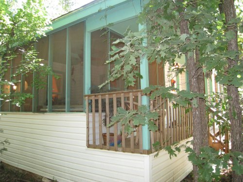 A small cabin with a screened porch, surrounded by trees and greenery.
