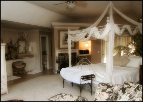 A cozy bedroom featuring a four-poster bed with draped fabric, a vintage chair, and soft lighting.