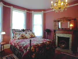 Cozy bedroom with floral bedding, a fireplace, chandelier, and large windows letting in natural light.