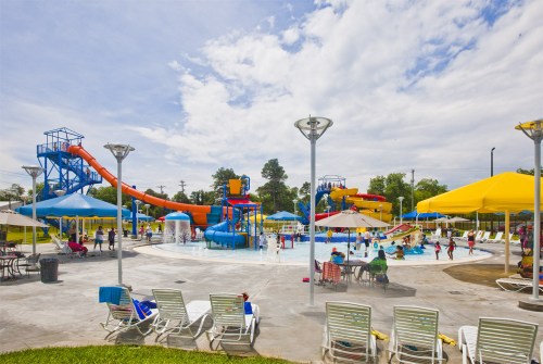A vibrant water park with slides, a splash area, and sun loungers under yellow umbrellas on a sunny day.