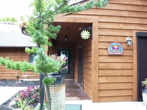 A wooden entrance to a lodge with a sign, surrounded by greenery and colorful flowers.