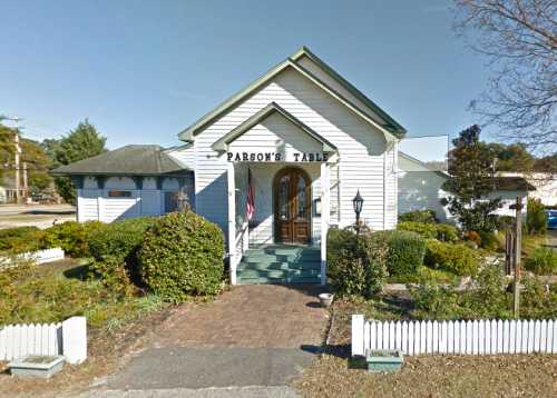 A white building with a green roof, labeled "Parson's Table," surrounded by greenery and a white picket fence.