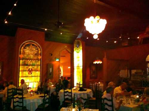 Cozy restaurant interior with stained glass windows, dim lighting, and diners enjoying their meals at elegantly set tables.