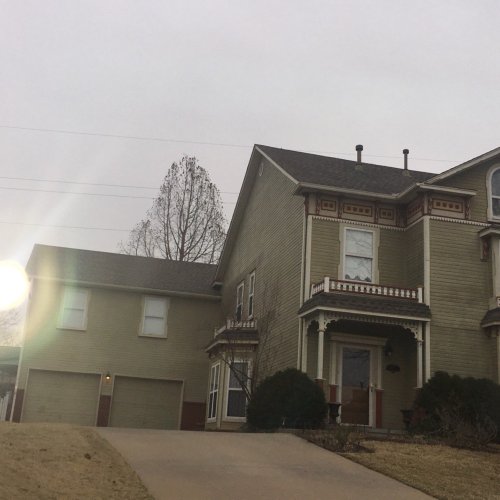 A large, two-story house with a porch, surrounded by trees, and a driveway leading to a garage.