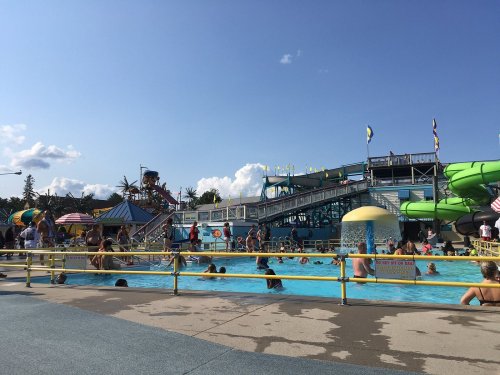 A busy water park scene with a pool, water slides, and people enjoying the sun on a clear day.