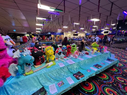 A colorful roller skating rink with a table of plush monsters and a vibrant patterned floor. People are enjoying the space.