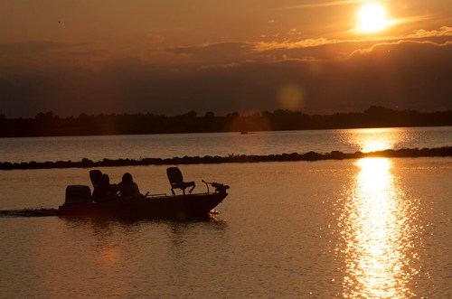 A silhouette of a boat with two people on a lake at sunset, reflecting golden light on the water.