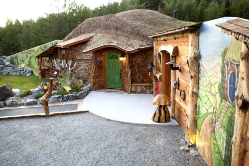 A whimsical, rustic house with a thatched roof, surrounded by nature and unique artistic decorations.