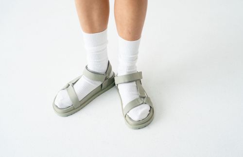 A pair of legs wearing white socks and green sandals on a white background.