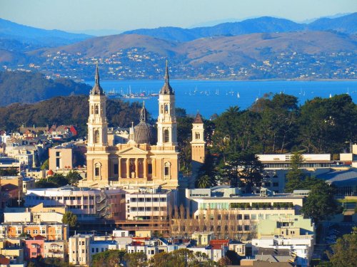 A scenic view of a city with a prominent church, mountains, and a bay in the background.