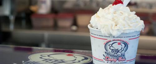 A cup of soft-serve ice cream topped with whipped cream and a cherry, placed on a counter at a dairy bar.