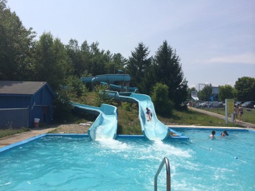 A sunny day at a water park featuring two blue slides and a swimming pool with people enjoying the water.