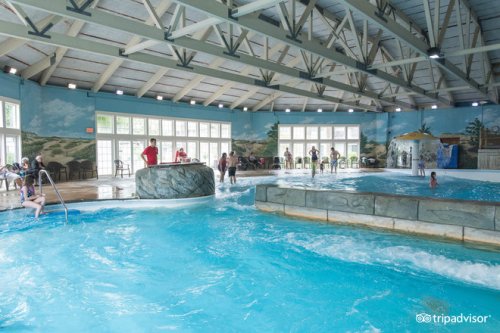 Indoor water park with a pool, rock formations, and people enjoying the water. Bright, spacious environment with large windows.