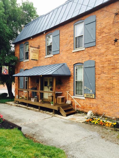 A brick building with blue shutters and a porch, featuring a sign for a bed and breakfast. Flowers line the walkway.