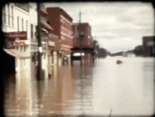 Flooded street with submerged buildings and debris, reflecting a severe water level rise in an urban area.