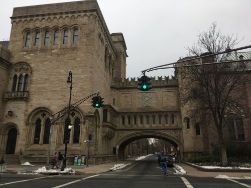 Historic stone building with an archway, green traffic light, and snow on the ground, set in an urban street scene.