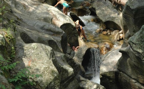 Two people play in a rocky stream, with water cascading over stones in a natural setting.