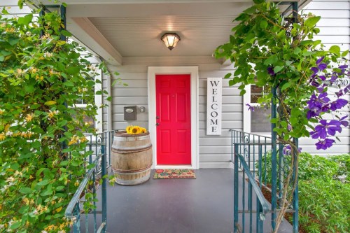 A welcoming entrance with a bright red door, potted flowers, and a decorative sign on a charming porch.