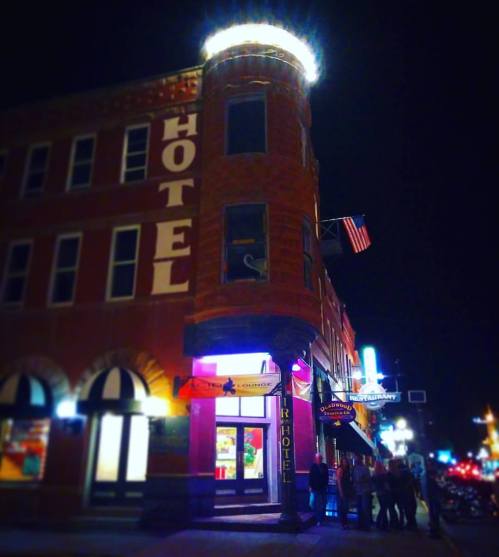 Historic hotel building at night, featuring bright lights and an American flag, with people gathered outside.