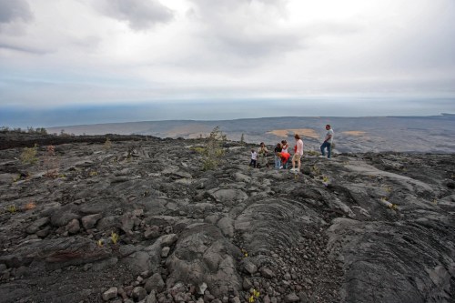 A group of people exploring a rocky volcanic landscape under a cloudy sky.