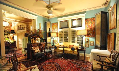 Cozy living room with blue walls, vintage furniture, decorative art, and a warm ambiance. A person stands in the background.