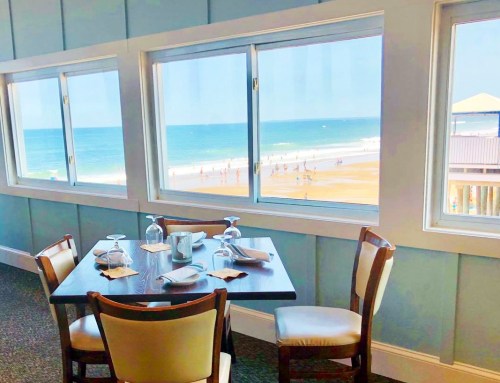 A beachside restaurant table with ocean views through large windows, featuring a serene beach scene outside.