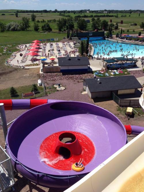 Aerial view of a water park featuring a large purple waterslide and a crowded pool area with umbrellas and sunbathers.