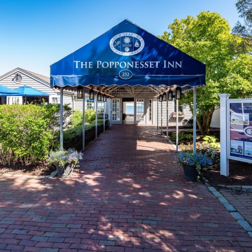 Entrance to The Popponesset Inn, featuring a blue awning and a brick pathway lined with flowers and greenery.