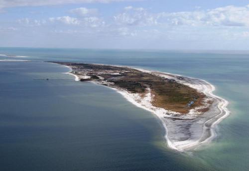 Aerial view of a sandy peninsula extending into a calm blue ocean under a partly cloudy sky.