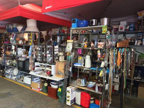 A cluttered thrift store display with shelves full of various household items and decorations.