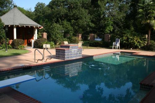 A serene backyard pool area with a gazebo, lush greenery, and lounge chairs under clear blue skies.