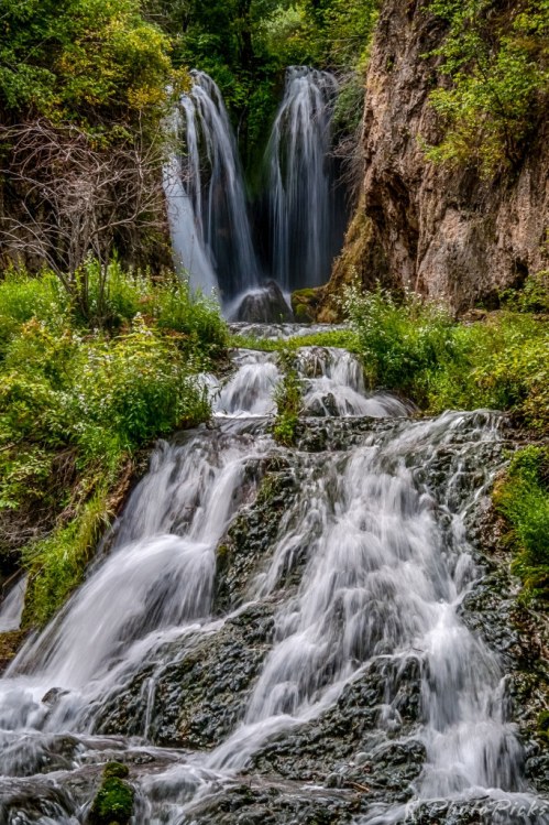 A serene waterfall cascading down rocky terrain, surrounded by lush greenery and vibrant foliage.