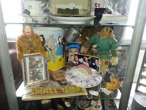 A display case filled with various collectibles, including dolls, photos, and memorabilia from "The Wizard of Oz."