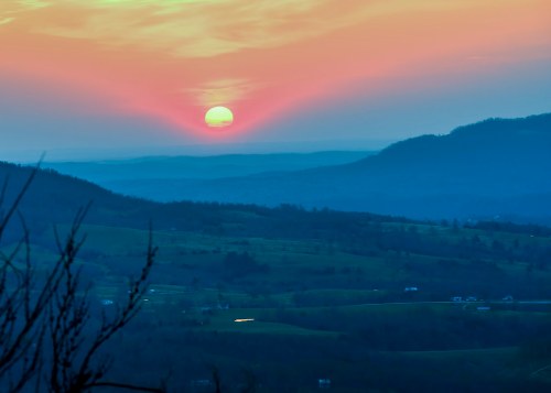 A vibrant sunset over rolling hills, with soft pink and orange hues illuminating the sky and landscape.
