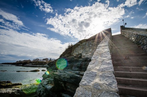 Stone steps lead up from the rocky shore to a scenic overlook under a bright, cloudy sky.