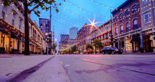 A charming street lined with shops, illuminated by string lights against a twilight sky.