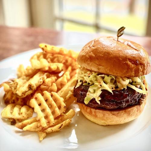 A juicy burger topped with coleslaw, served with crispy waffle fries on the side.