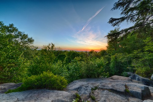 A scenic view of a rocky landscape with lush greenery and a colorful sunset in the background.