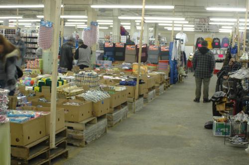 A bustling indoor market with rows of boxes filled with various goods and shoppers browsing the aisles.