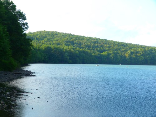 A serene lake surrounded by lush green hills under a clear blue sky.