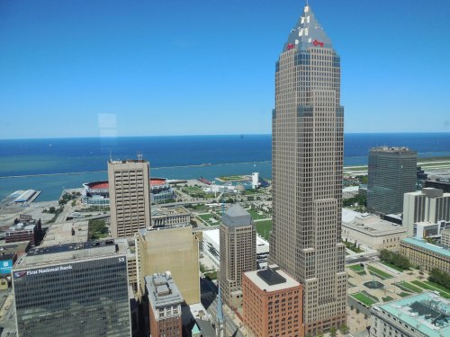 Aerial view of downtown Cleveland, featuring skyscrapers and Lake Erie in the background under a clear blue sky.