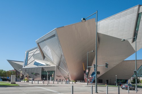 A modern, angular building with reflective surfaces and a clear blue sky in the background.